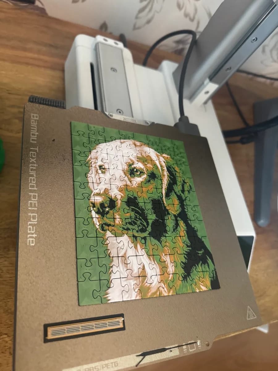 A small 3D printed photo puzzle of a dog in green and white, fresh on the printer's build plate