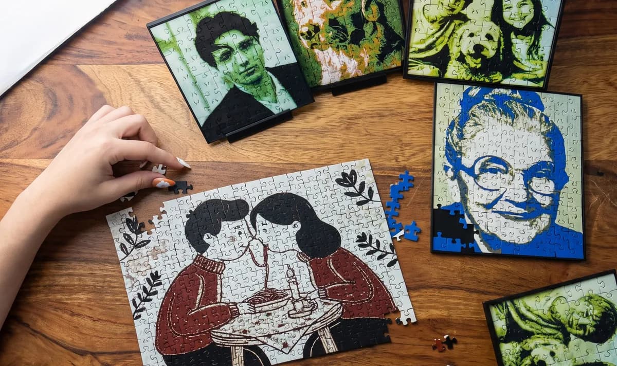 Several 3D printed photo puzzles on a wooden table: a man's portrait in green, a grandmother in blue, kids with a dog, and an illustrated couple being assembled by hand